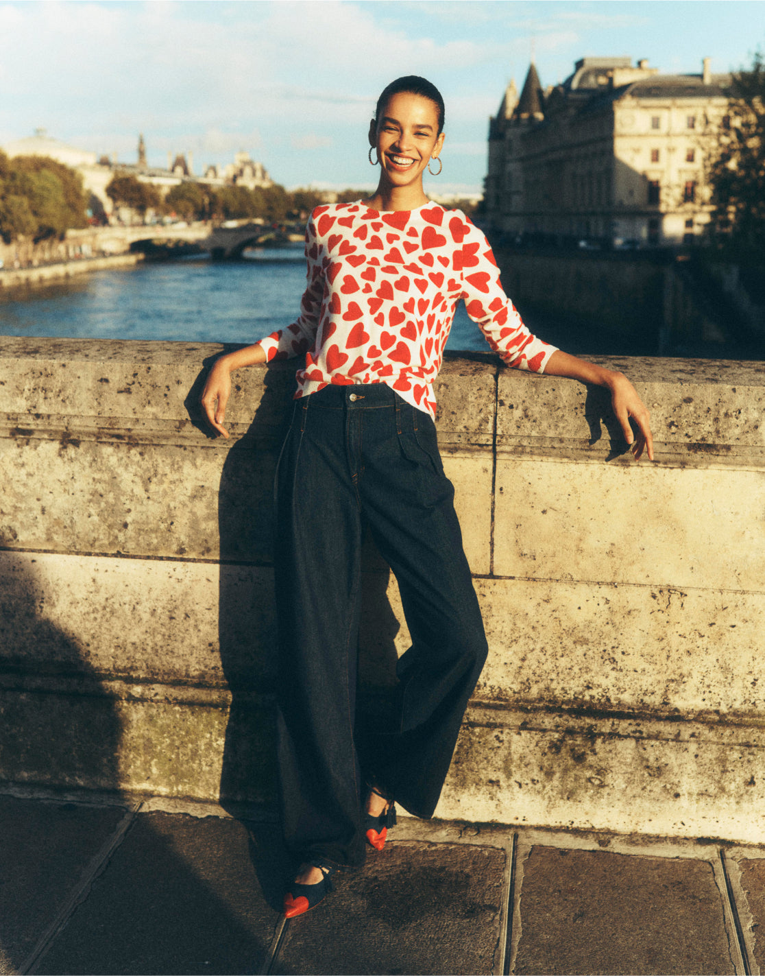 Woman stood on a bridge in Paris wearing a Boden love heart jumper