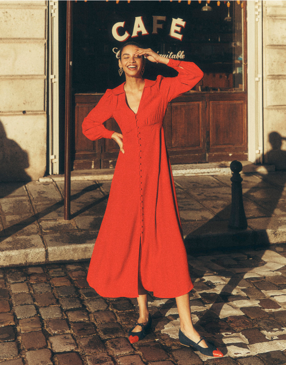 Woman stood outside a café in Paris wearing a red Boden dress