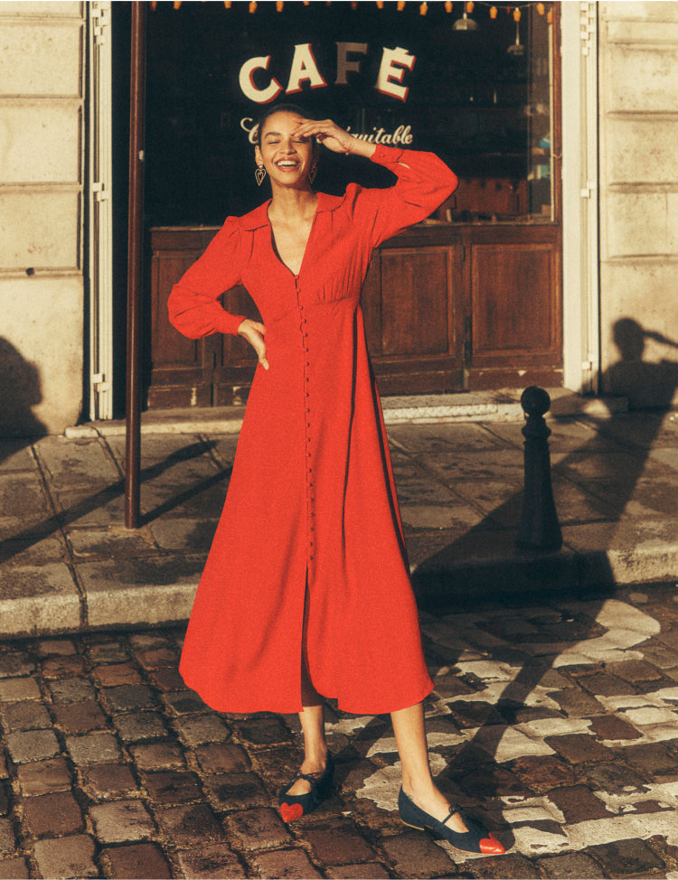 Woman stood outside a café in Paris wearing a red Boden dress